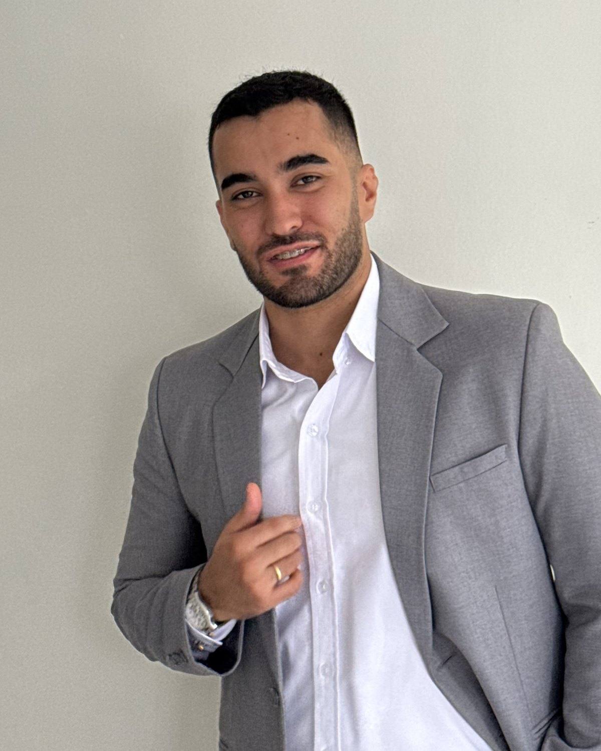 Elian Camilo, sonriendo, con saco gris y camisa blanca